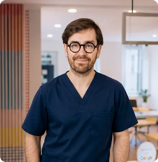 Portrait d'un praticien souriant à lunettes, en tenue bleu marine